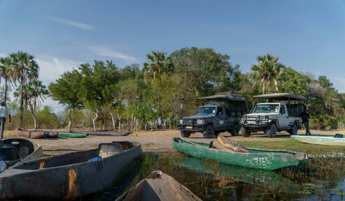 Two safari vehicles parked by a lake with canoes